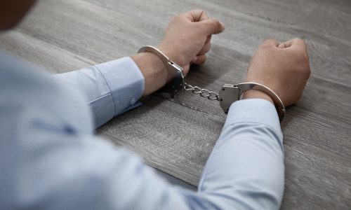 A selective focus shot of male hands in handcuffs on a wooden table